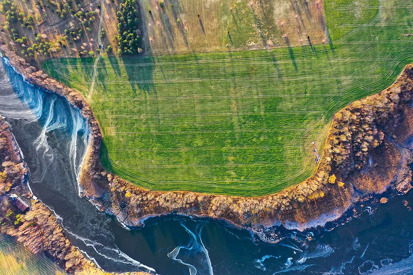 Riverbank with ice and a green field, view straight from above
