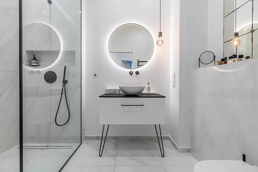 White bathroom with a shower and a round lit mirror