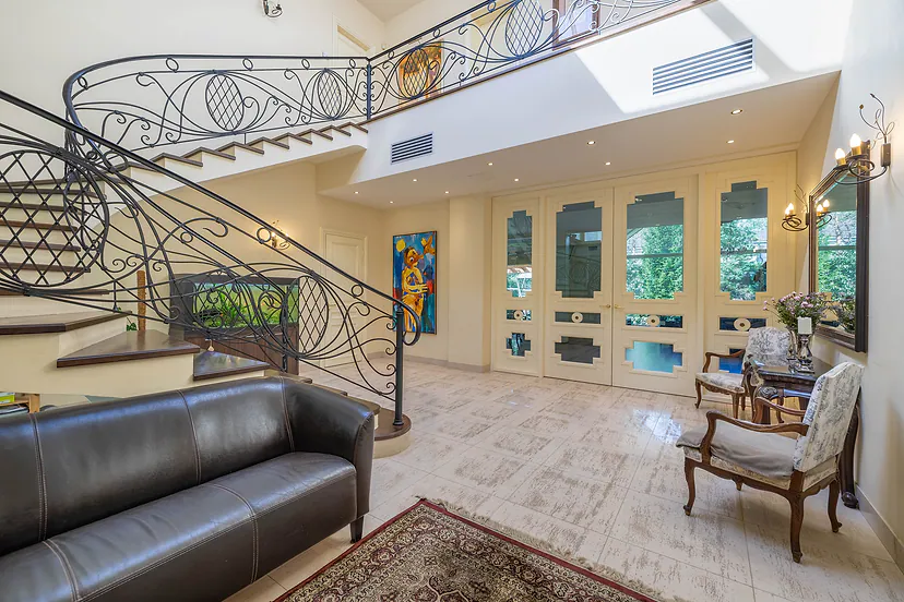 Spacious hall with curved stairs, wrought iron railings and a leather sofa