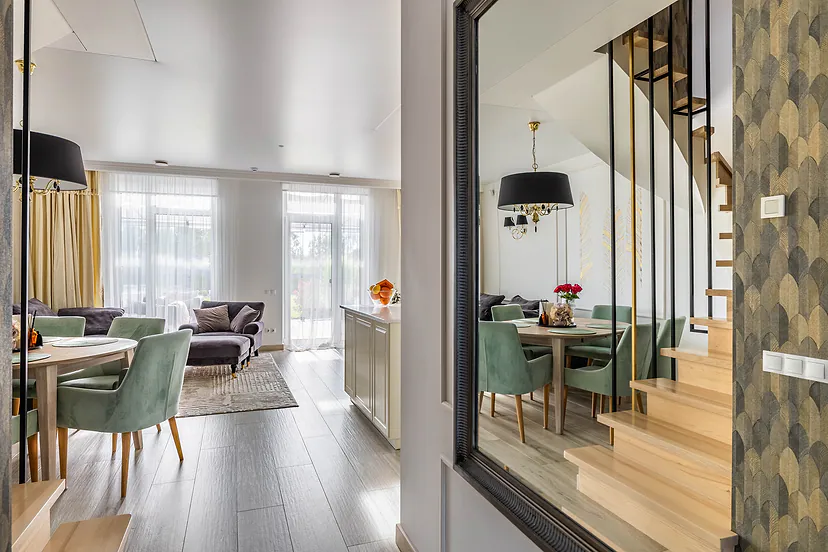 Living and dining room with green chairs, wooden stairs and a large mirror beside them