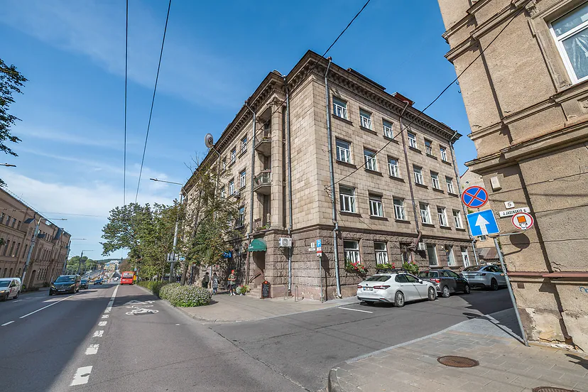 Senas mūrinis pastatas gatvės kampe saulėtą dieną