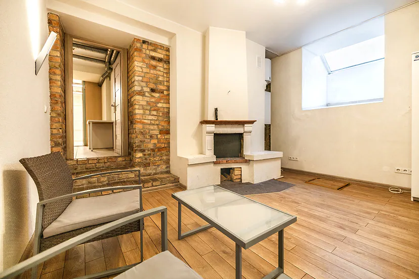 Room with a white fireplace, an exposed brick wall and wooden floors