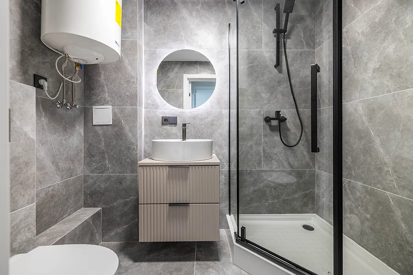 Bathroom with grey tiles, a shower cubicle and a round mirror