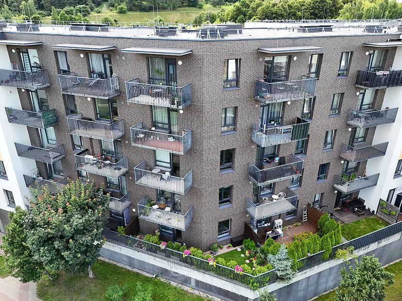 Brick apartment building facade with balconies and a yard, photographed by drone